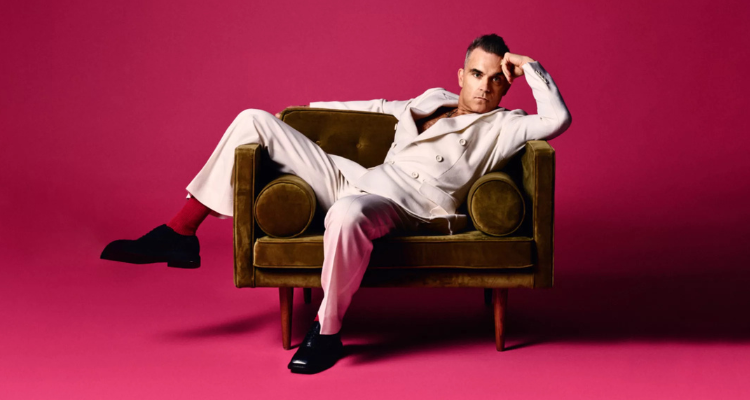 Robbie Williams on a sofa with a pink background.