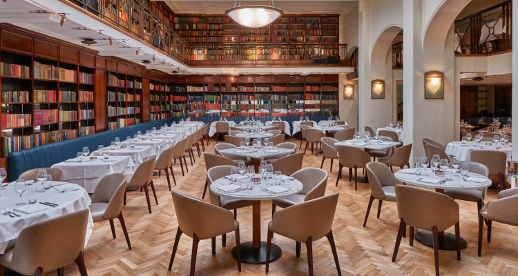 Interiors of Cinnamon Kitchen Westminster, featuring elegant tables, parquet floors and walls lined with books.