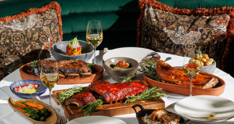 Grilled meats and fish alongside a spread of vegetables from Amazonico's feast menu, presented in a velvet green booth on a white tablecloth-clad table.