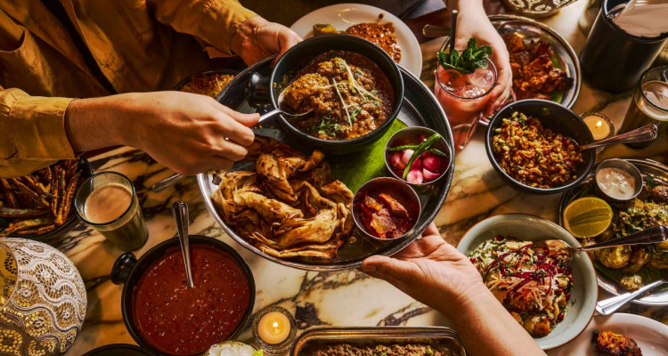 Dishes of Bombay-inspired food being passed across the table by a group sitting down for Dishoom's feasting menus.