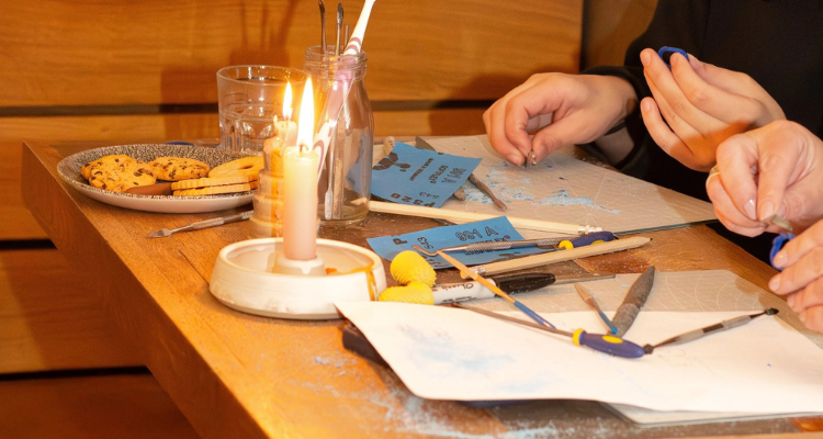 People crafting lost wax rings at a table with cookies and a candle.