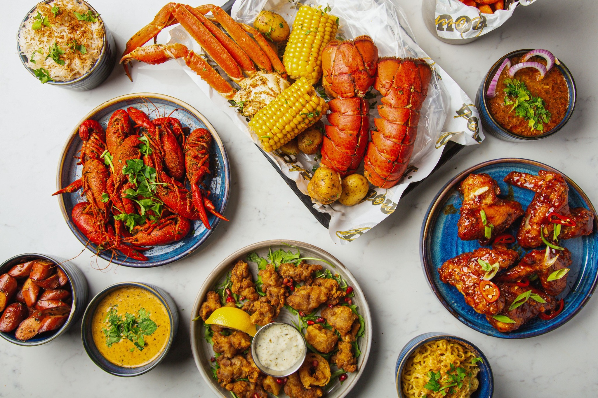 Seafood boil at Hot N Juicy Shrimp, including lobster, crab and corn, alongside a few side dishes such as chicken wings and rice.