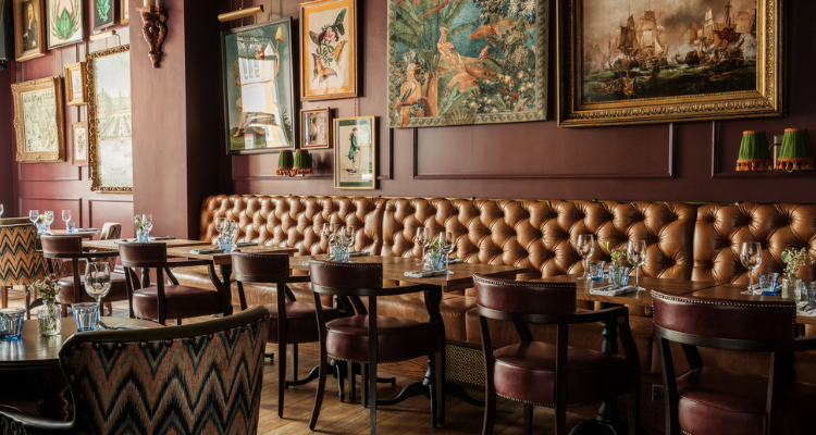 A picture of The Trafalgar's oxblood-coloured interiors, fronting quirky works of art and green lamps.