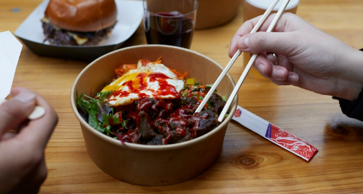 A photo of a hand holding chop sticks in front of a Korean rice bowl.