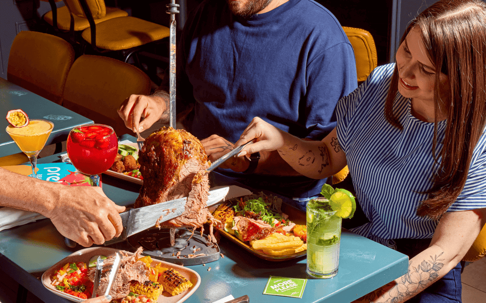 People at Preto Brazilian Barbecue Restaurant enjoying a rodizio experience, including meat skewers carved at their table.