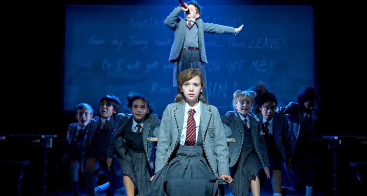 Children singing and dancing with desks at school in Matilda the Musical.