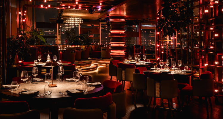 A picture of CÉ LA VI London's lavish interiors, fronting glass artwork, red interiors and circular tables.
