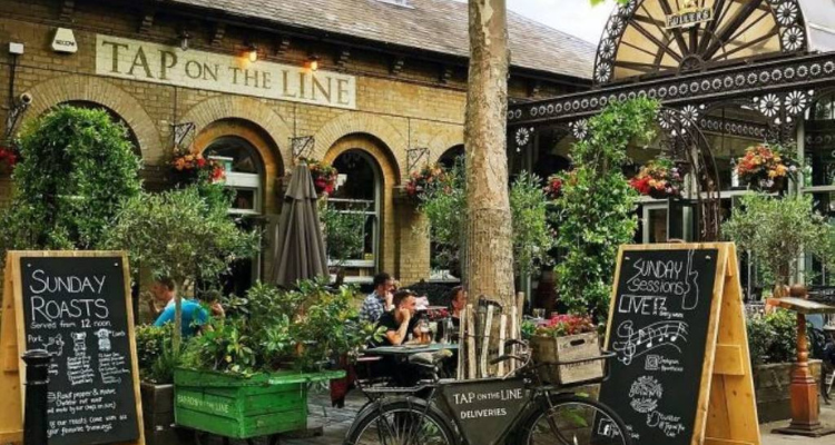 The exterior of Tap On The Line, featuring a small beer garden and signage.