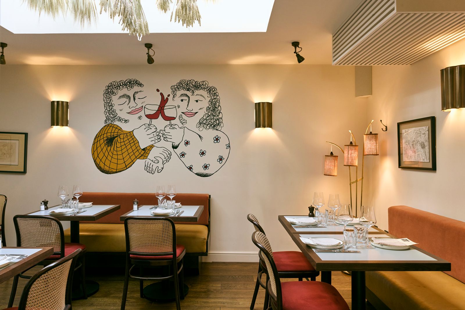 Interiors at Elsa in Fitzrovia, featuring banquette seating, wooden tables, and a fun wall mural of people drinking wine.
