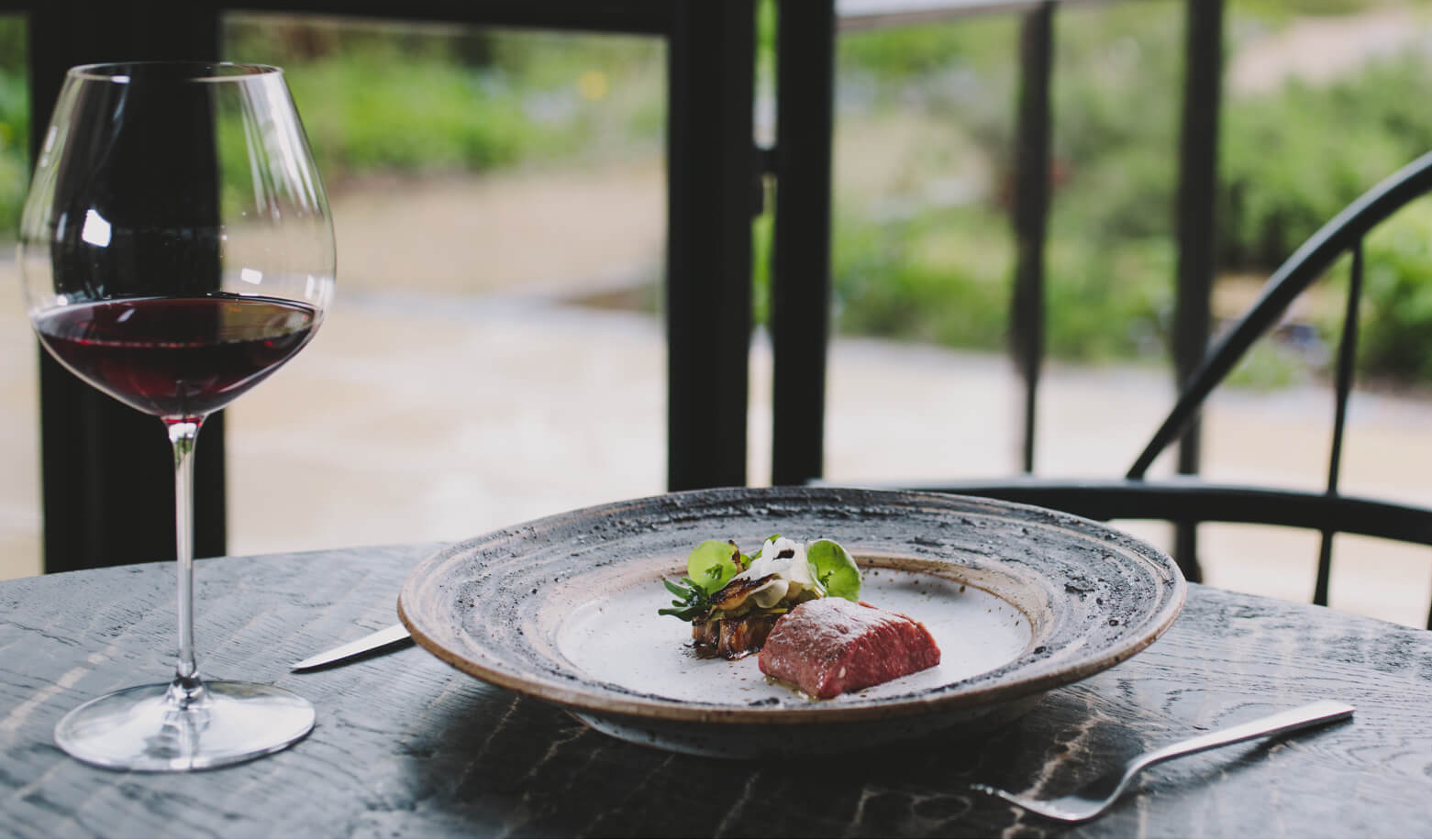 Glass of red wine and meat dish by the window at Grace & Savour Birmingham.