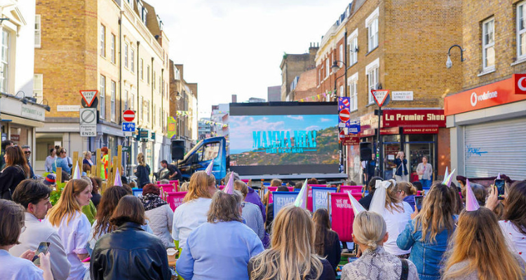 People gathered outdoors to watch Mamma Mia on an outdoor cinema screen.