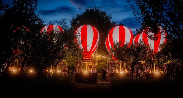 A fleet of anchored hot air balloons lit up by twinkling lights in the evening.
