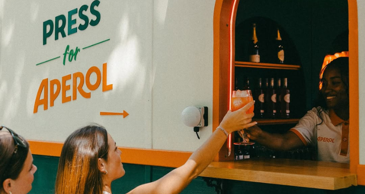 An Aperol Spritz window with a cocktail being handed to a woman.
