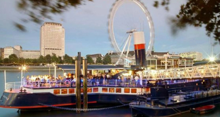 A docked boat packed with people in London with a view of the London Eye.