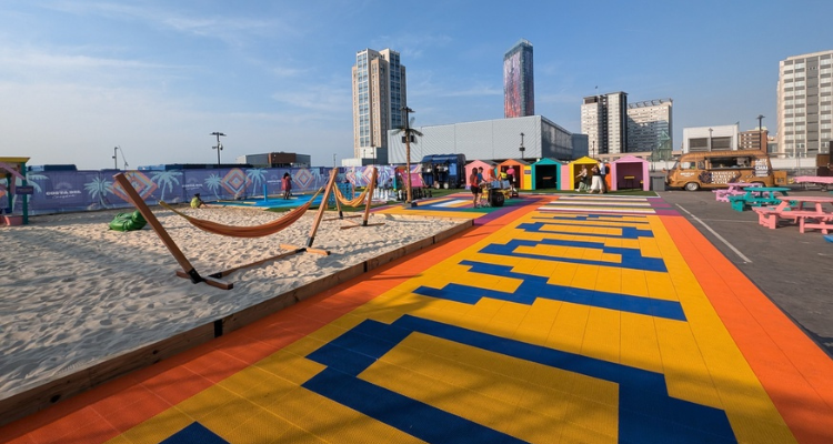 A car park transformed into a beach with sand, hammocks, and bright pink benches.