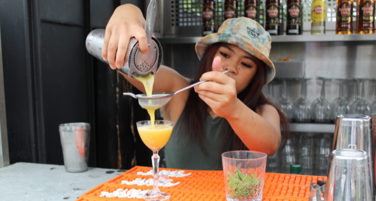 A bartender pouring a yellow cocktail into a glass.