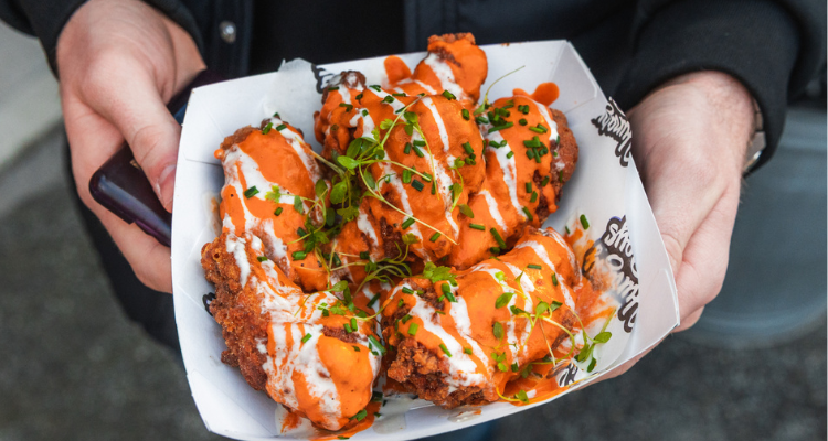 Someone holding a street vendor box filled with chicken wings.