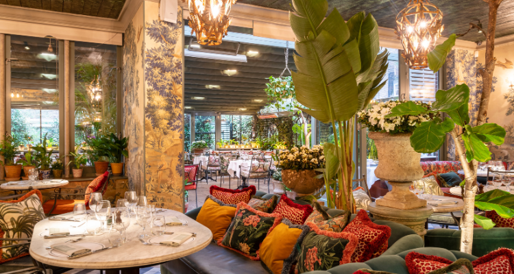 A picture of The Ivy Chelsea Garden's stunning interiors, including lush green plants, patterned wallpaper and red cushions.