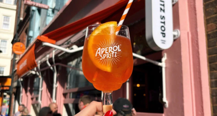 An Aperol Spritz being held up in the sun.