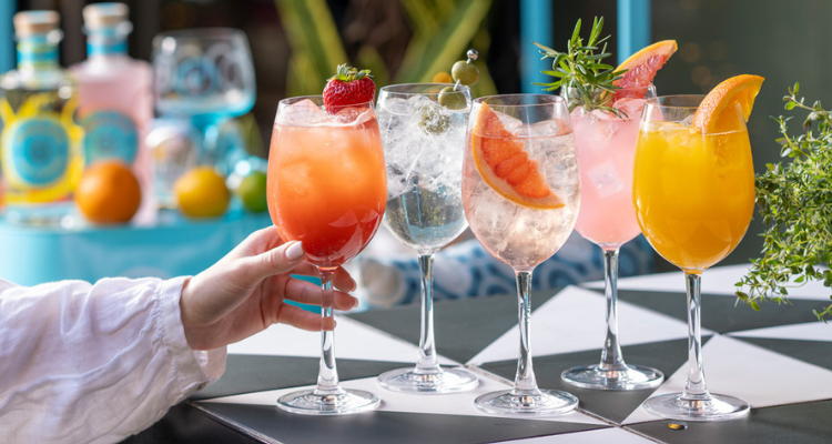 Four glasses with colourful summer spritz drinks.