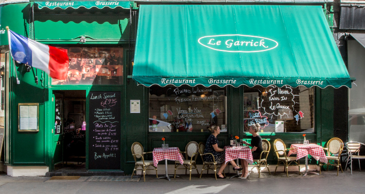 The exterior of a French restaurant with a chalk board sign and outdoor seating.