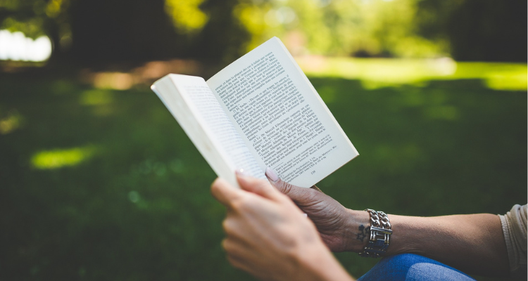 Someone holding and reading a book in a park.