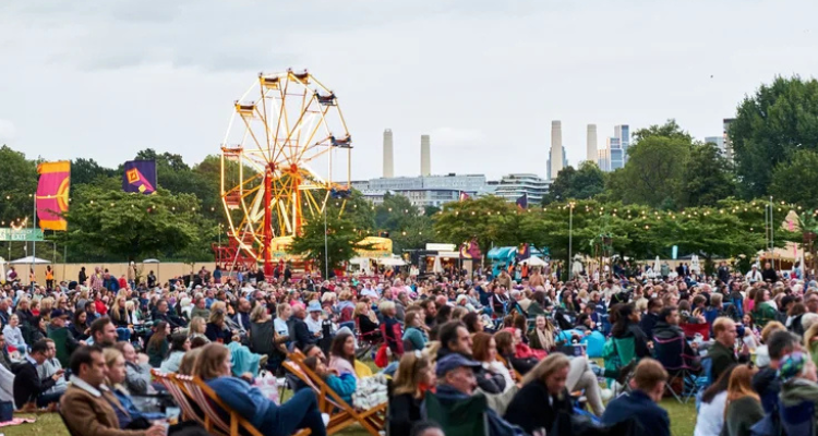 A crowd of people seated in lawn chairs in a park with a Big Wheel in the back.