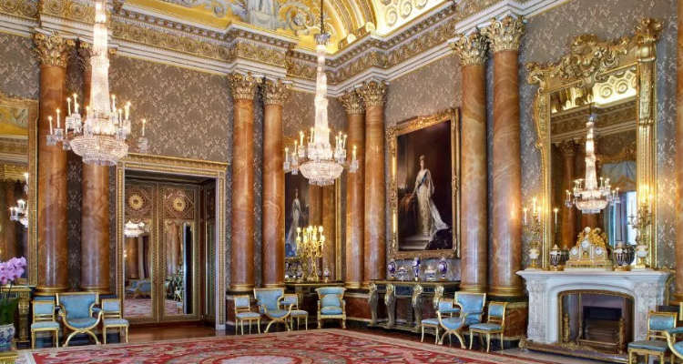 The inside of Buckingham Palace with chandeliers, grand pillars, gold mirrors, and art work.