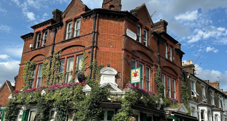 The leafy exterior of a brick pub on a clear day.