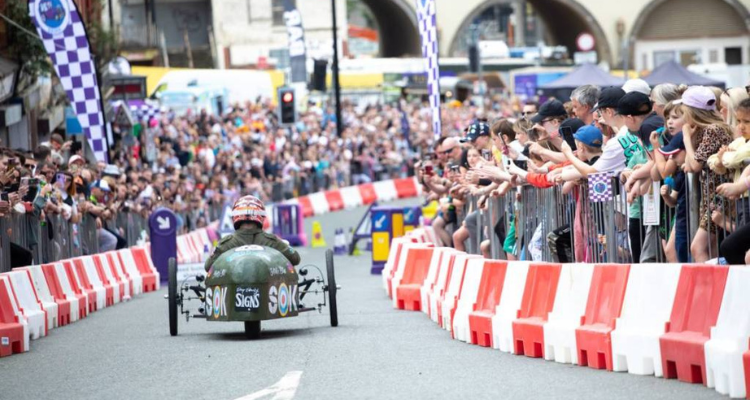 A homemade soapbox racing downhill as hundreds of spectators watch and cheer.