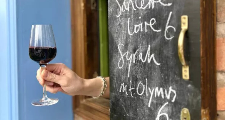 A hand reaching through a wooden hatch with a glass of red wine.
