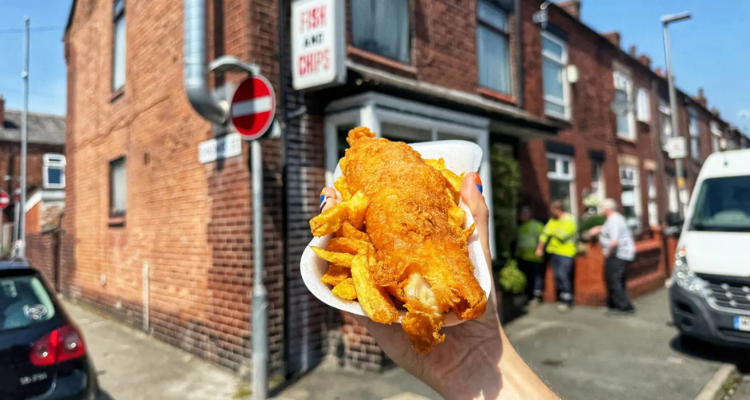 A hand holding fish and chips outside of a residential home.