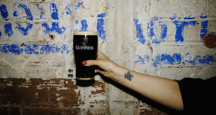 A hand holding a pint of Guinness against a blank wall.