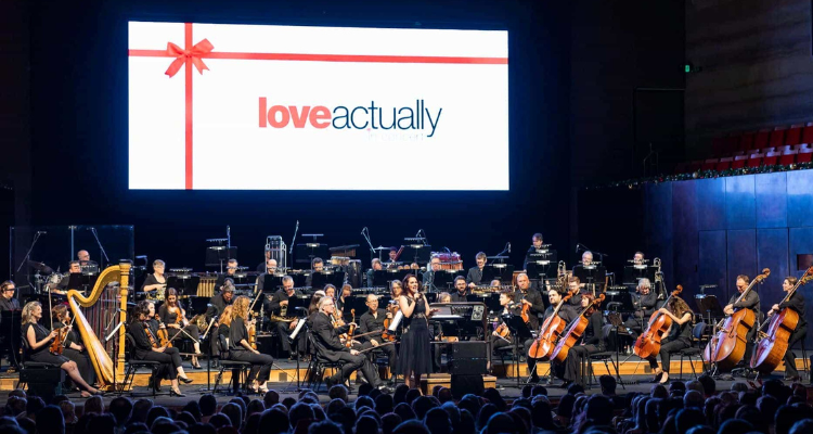 A large cinema screen showing Love Actually with an orchestra below.