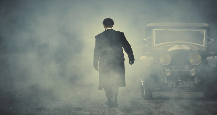 A still from the Peaky Blinders where a man in a long coat is walking away.