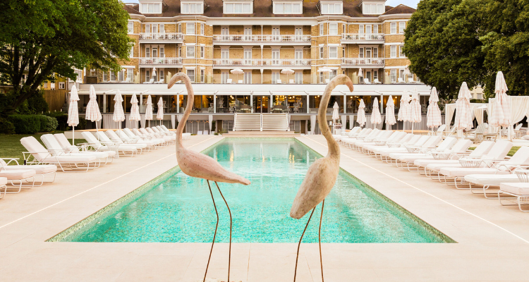 A chic Miami-inspired pool in front of a glamorous hotel with 2 flamingo statues and sun loungers.