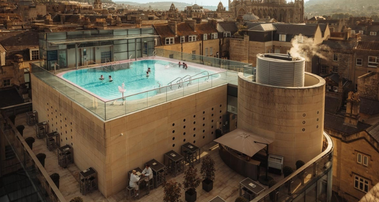 People taking a dip in a rooftop pool overlooking the city of Bath.