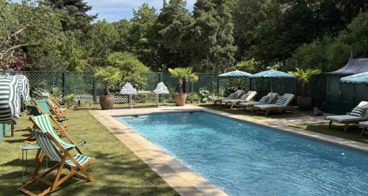 A small pool surrounded by grass, sun loungers, and trees.