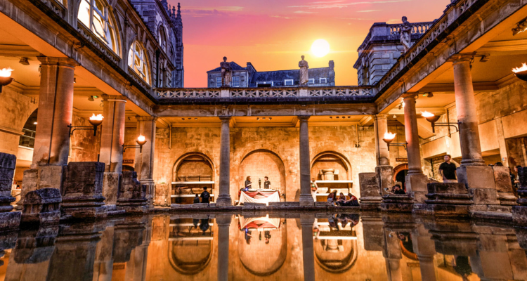 The sun setting over the Roman Baths as people explore inside.