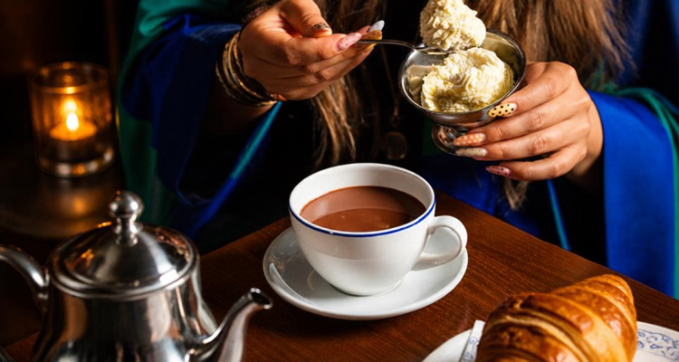 Someone spooning whipped cream into a hot chocolate at a cafe.
