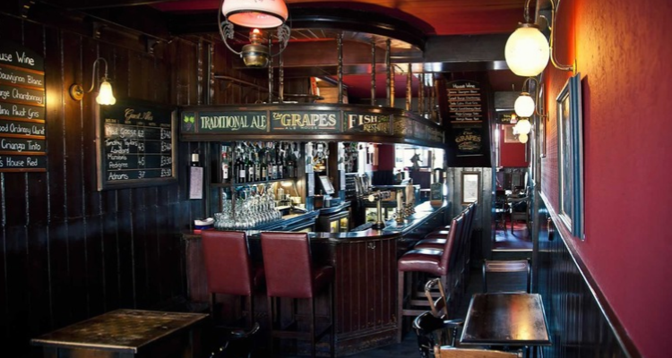 The interior of The Grapes, featuring red walls, a chalkboard, and a classic no-frills pub interior.