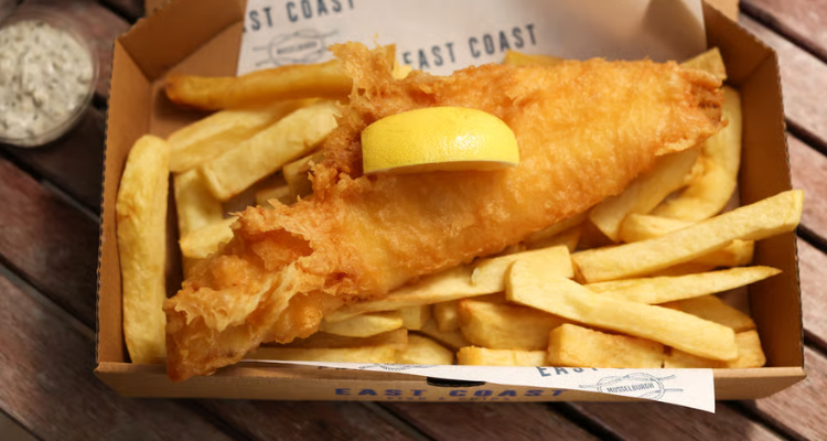 Fish and chips in a takeaway box with a lemon on top.