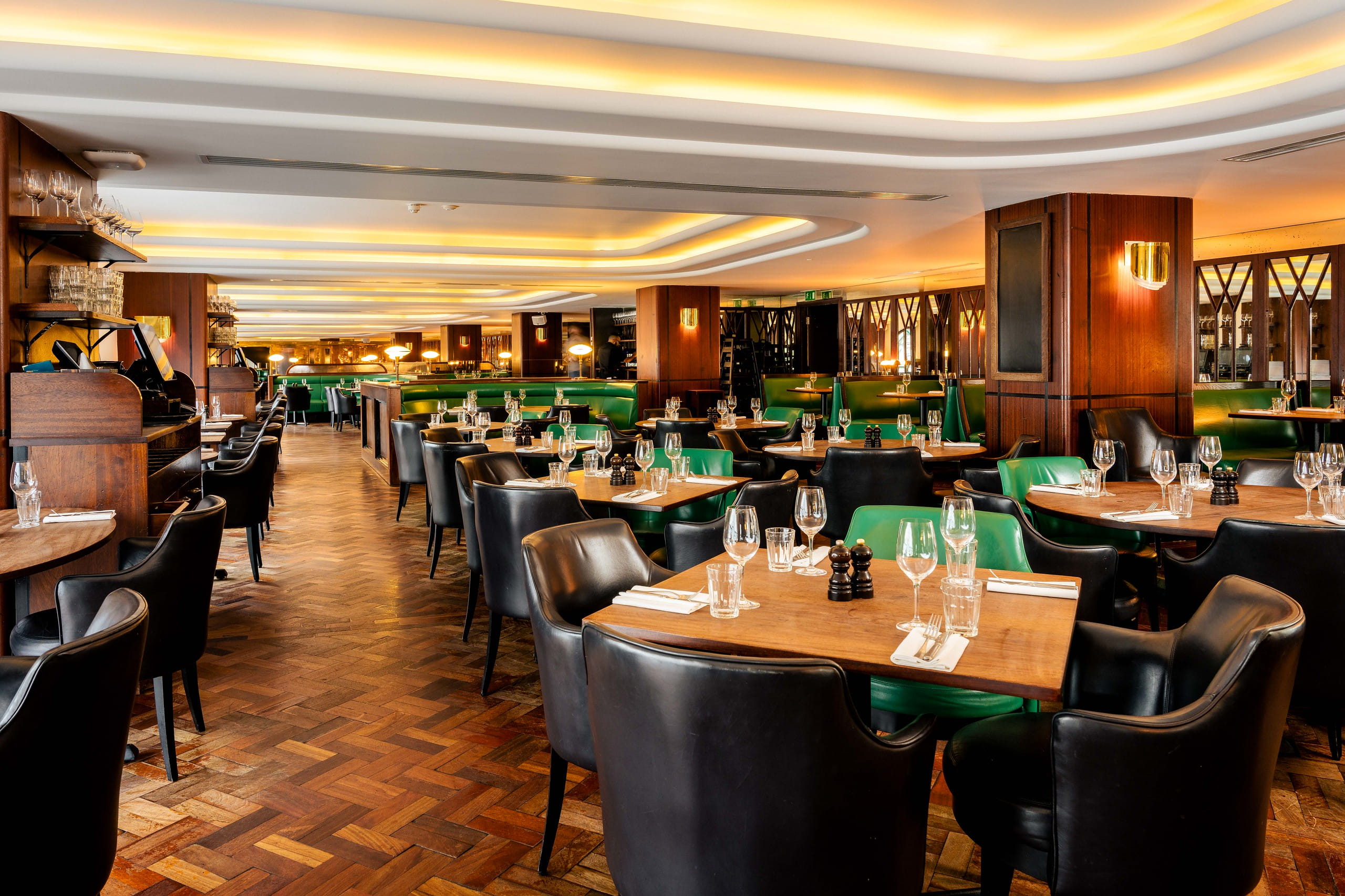 Dining room at Hawksmoor Air Street, featuring wooden parquet floors, leather seating and warm lighting.