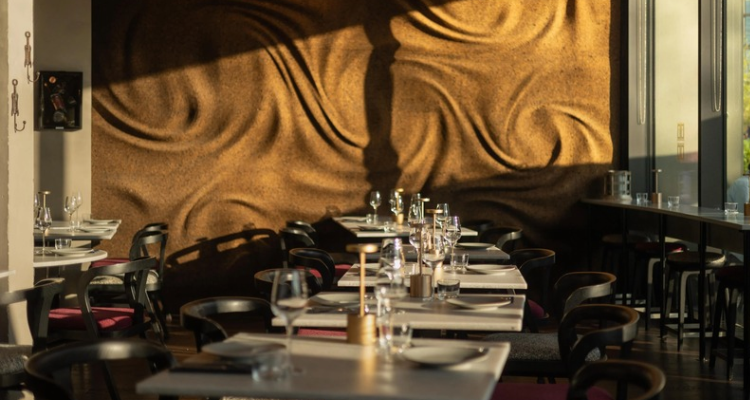 The interior of Porte Noire featuring a textural wall, empty tables ready for dinner service, and wine glasses.